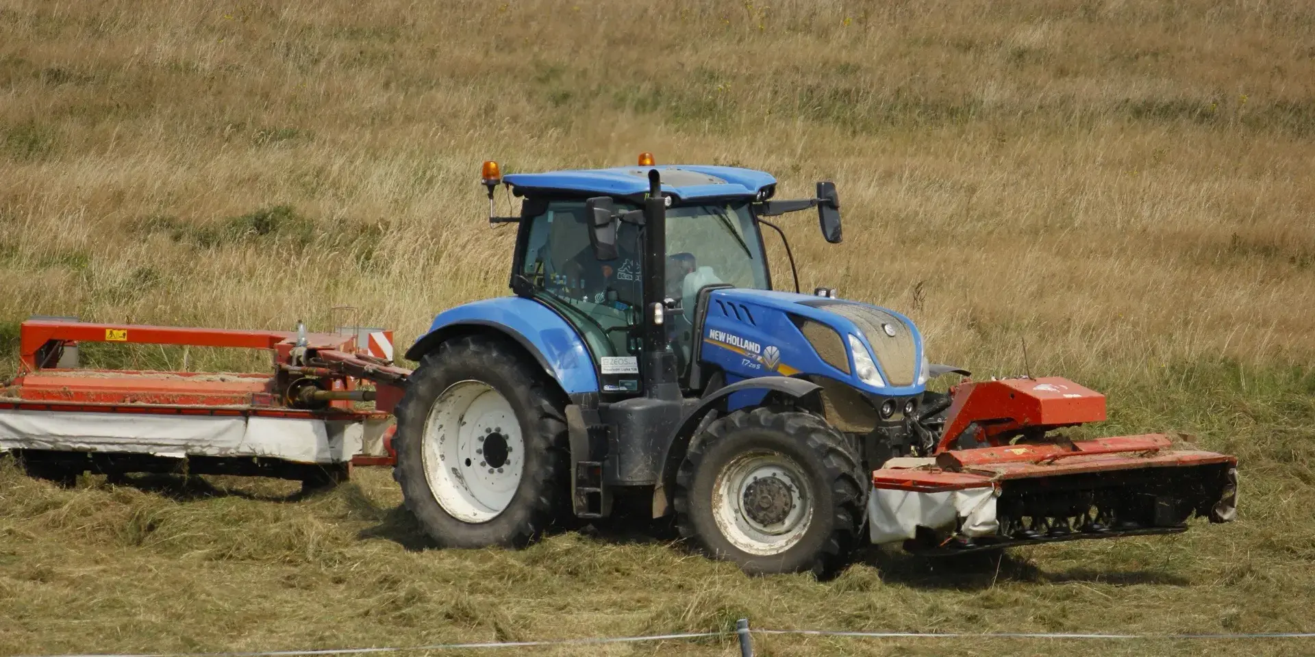 New Holland trekker met maaicombinatie aan het werk op grasland