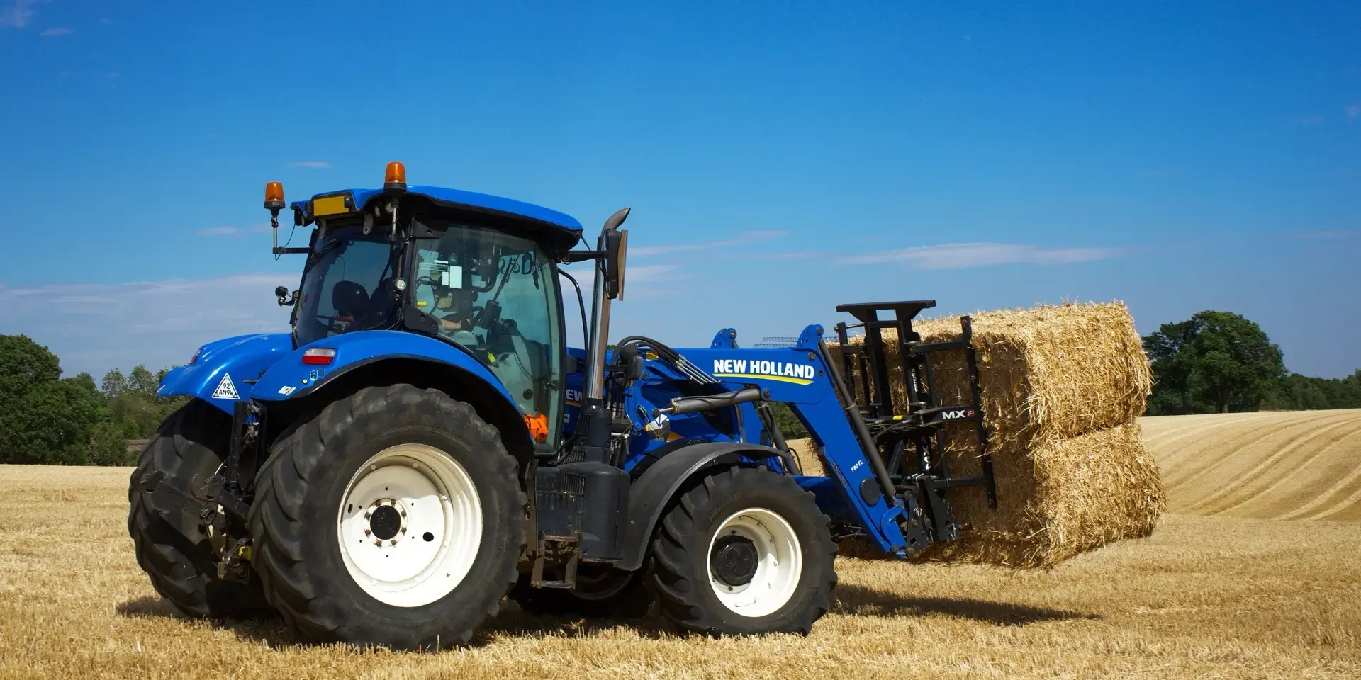 New Holland trekker met voorlader en strobalen op het land